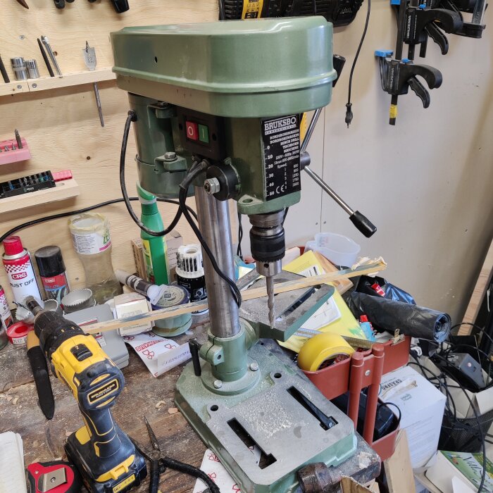 Grön Bruksbo pelarborrmaskin placerad på en arbetsbänk med olika verktyg i bakgrunden.