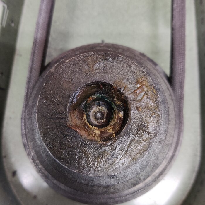 Oljesmutsig mekanisk del sedd ovanifrån med slitage och smuts runt centrum.