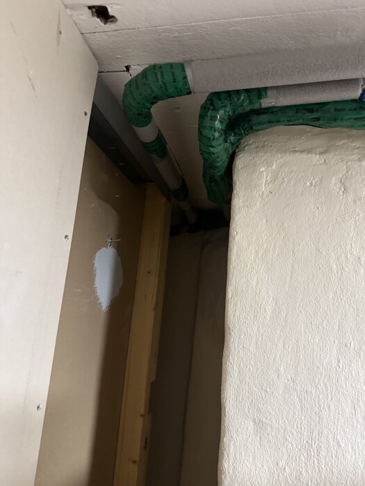 Isolerade vattenrör inomhus, grönt täckmaterial, väggar runt omkring. Förberett för att undvika kondens och planerar inspektionsluckor.