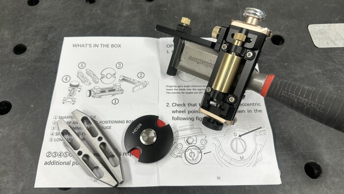 Verktyg för slipning av stämjärn, inklusive en slipjigg och skala. Manual med komponentdiagram i bakgrunden.