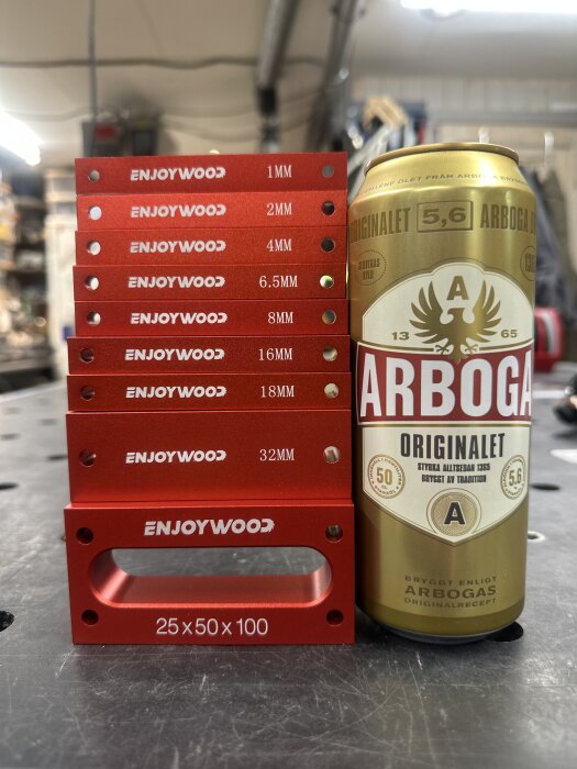 Röda måttsatsblock från Enjoywood i olika storlekar, bredvid en burk Arbogabrygd öl, på ett verkstadsbord.