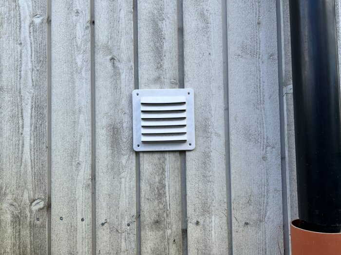 Väggpanel med monterad ventil och avsågat svart rör intill, del av färdigställt byggprojekt.