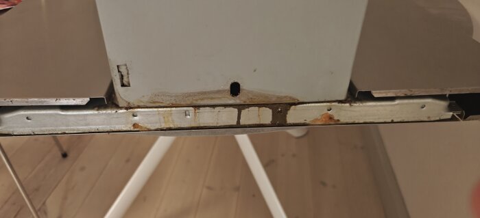 Köksfläktens undre del med rost och smuts efter demontering, synlig metalldel och skruvhål.