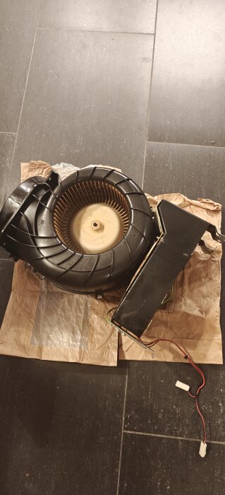 Köksfläktsdelar med synliga fläktblad och motor, liggande på golvet för rengöring eller demontering.