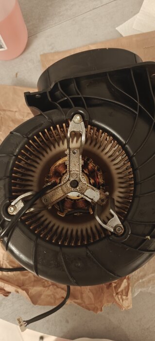 Delar av en isärplockad köksfläkt, med synliga metallkomponenter och fläktblad fortfarande monterade på motorn.