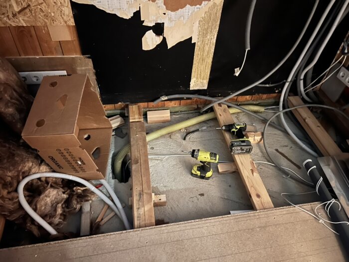 Byggarbetsplats i barnrum med verktyg, kablar och en kartong, väggar delvis öppnade för renovering och kabeldragning.