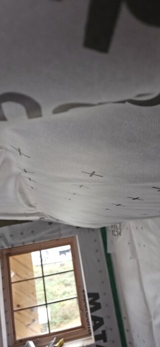 Isolering och ångbroms i en friggebod som sviktar nedåt, med ett fönster i bakgrunden.