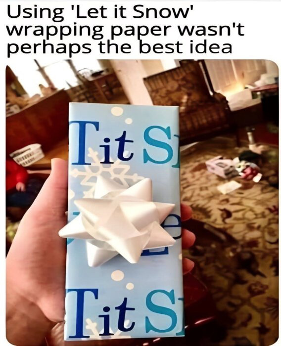 En julklapp inslagen i papper med "Let it Snow", men texten syns som "Tit", pga placering. Vit rosett ovanpå.