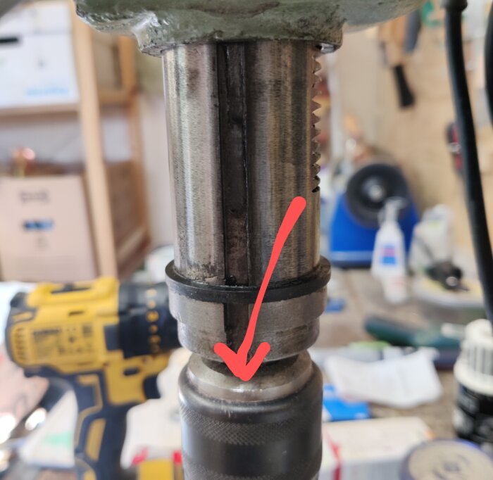 Borrmaskin med trasig chuck markerad med röd pil i verkstadsmiljö.