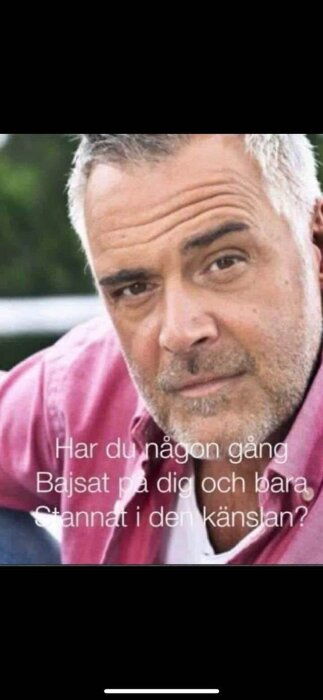 En man med skäggstubb i rosa skjorta med text om bajsa på sig och känslan som uppstår.