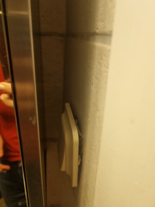 Ett löst lamputtag håller på att lossna från väggen, med synlig glipa längs kanterna.