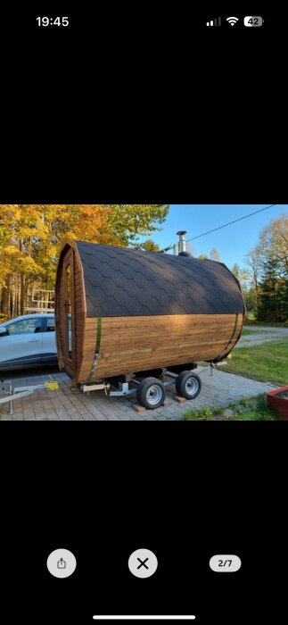 Bastuvagn monterad på en släpvagn stående på stenlagd uppfart, omgivet av träd i höstfärger.