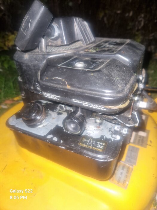 Närbild av en gräsklipparmotor med fokus på primerblåsan. Text på motorn säger "Push to Prime" med instruktion att trycka tre gånger.