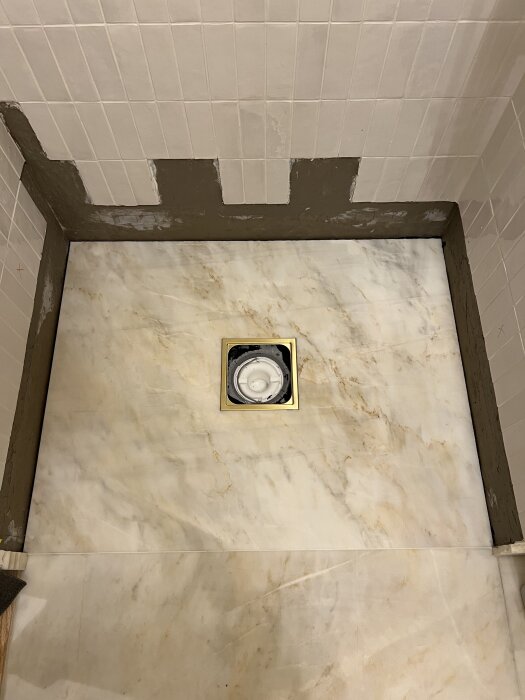 Ny marmorplatta installerad i dusch med tveksam fog runt avlopp; slipat fall på 9 mm. Flera gropar och vrår i fogen synliga.