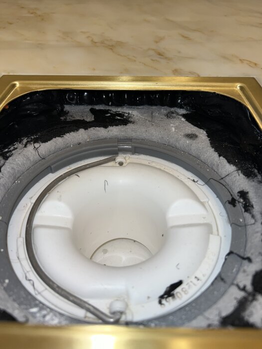 Nära bild av duschbrunn med marmorplatta runtom, visar ojämnt fogarbete och flera gropar kring brunnen.