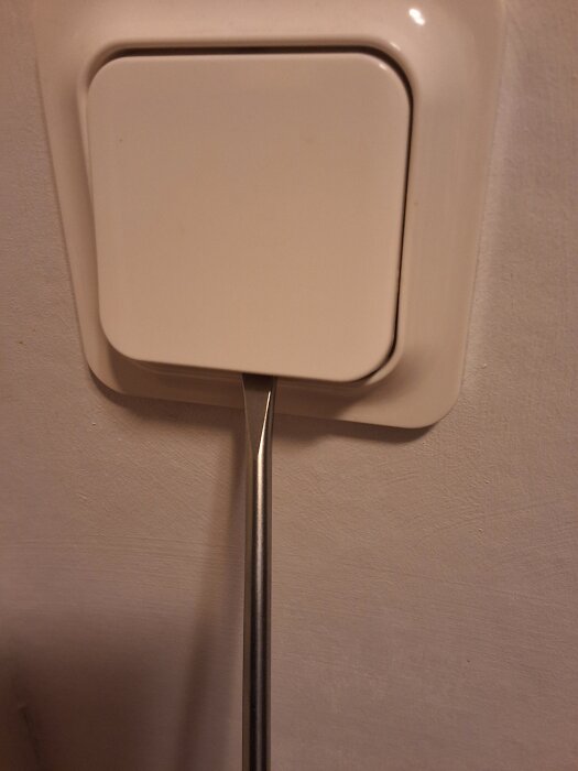 Skruvmejsel används för att lossa en vit väggknapp genom att placera den under knappens nederkant.