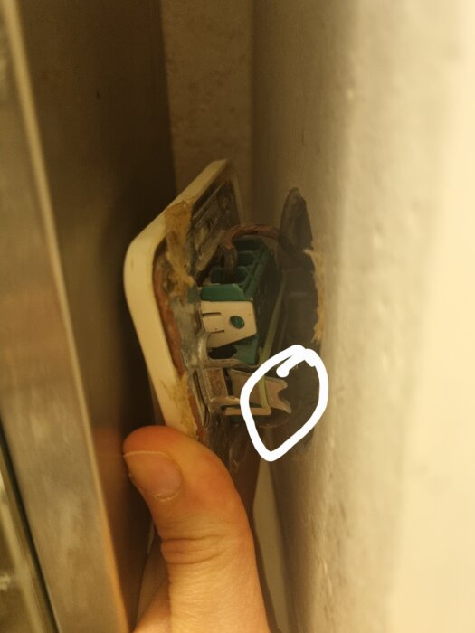 Löst sittande strömbrytare på väggen med synliga ledningar, en person håller den och en oregelbunden detalj är markerad med en vit cirkel.