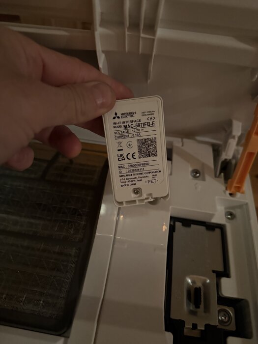 En hand håller ett WiFi-interface av modellen MAC-597IFB-E från Mitsubishi Electric, med etikett där specifikationer syns.