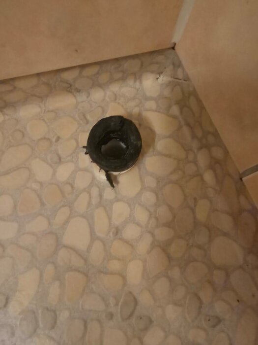 Avloppshål i mosaikgolv med rustikt utseende, behov av installation av spilltratt för tvättmaskin.