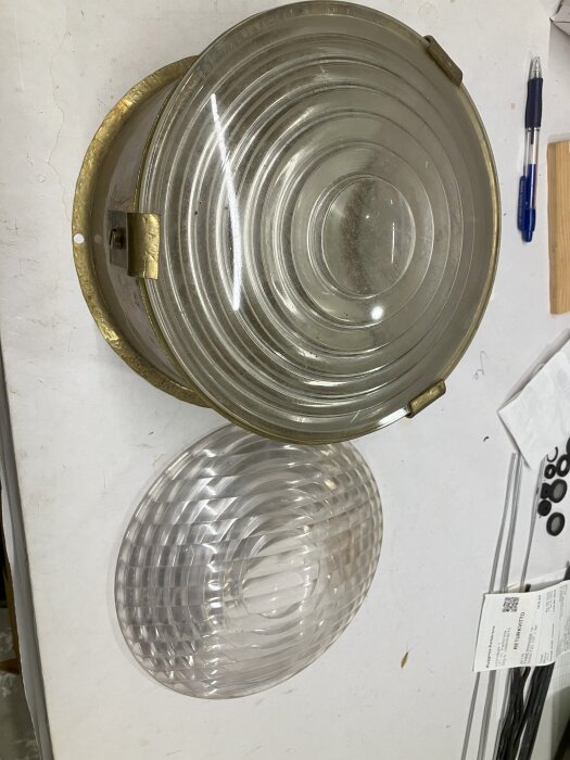 Fresnel-linser, en glaslins i mässing och en plastlins med sidobrytningsfält, ligger på ett bord med papper och penna bredvid.