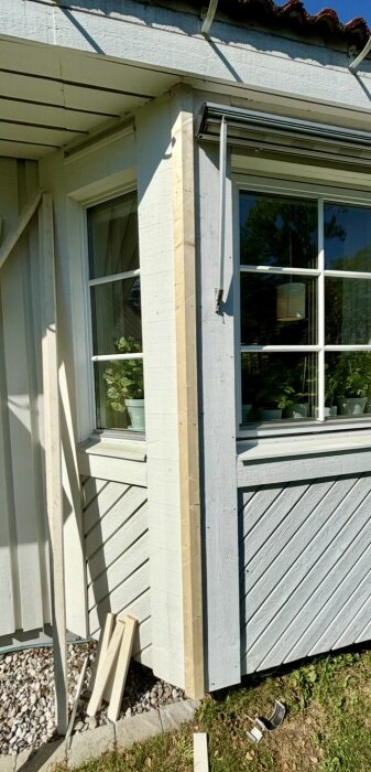 Hyvlade reglar monterade på en husfasad med vita fönster, del av ett byggprojekt med sågade träbitar i förgrunden.