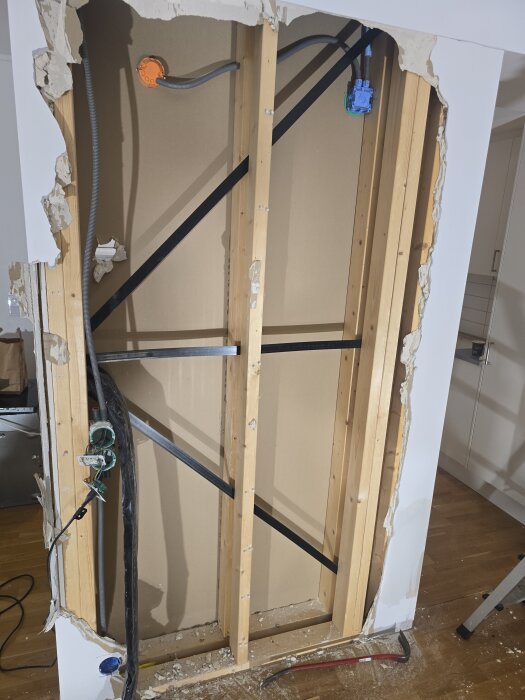 Öppen vägg med träreglar, synliga kablar och rör på trä- och gipskonstruktion, delvis borttagen gipsvägg, stång på golvet.