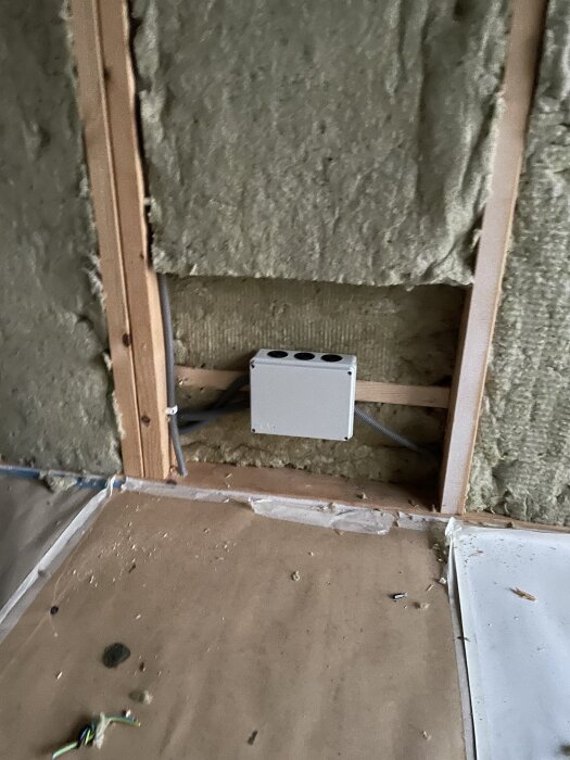 Vägg med isolering och en elektrisk kopplingsbox placerad utanför en framtida bastu. Golv av täckpapper och synliga kablar.