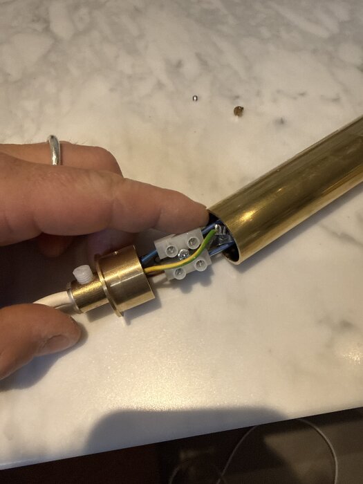 Hand håller i en lampa med exponerade kablar och kopplingsdel på en marmoryta.