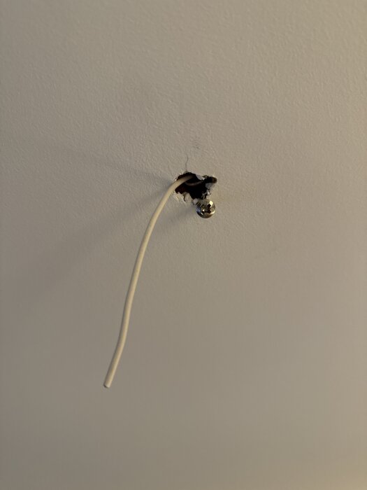 Gammalt VP-rör i taket med synlig RKK-kabel hängande ut genom ett litet hål i vitmålad yta.