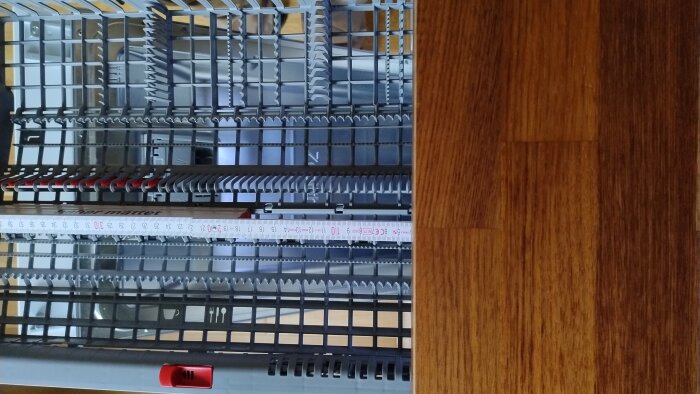 Diskmaskinens övre korg med en mätsticka synlig i förgrunden för att visa avstånd eller justering. Korgen har olika fack och detaljer.