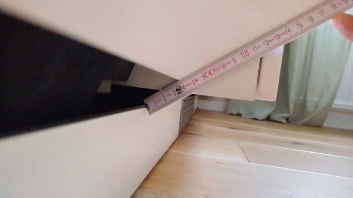 Mätning av avståndet mellan diskmaskinens lucka och sockel med ett måttband, sedd från sidan med halvöppen lucka.