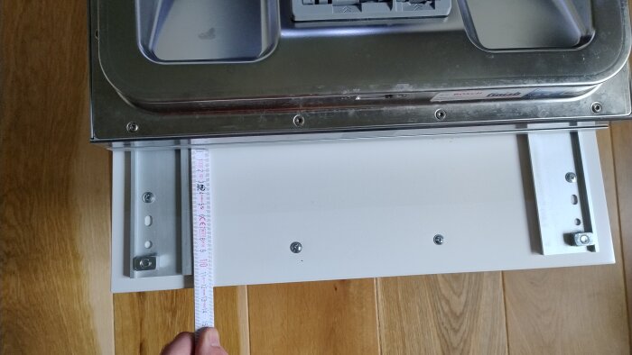 Diskmaskinslucka halvöppen, med en person som mäter avståndet från skåpets ovansida med ett måttband.