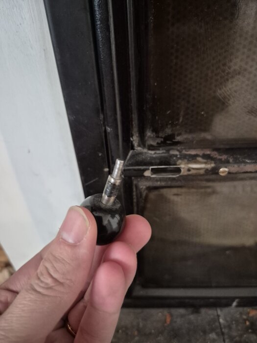 Knapp som ska limmas tillbaka på en braskamins dörr, visas av en hand framför kaminen.