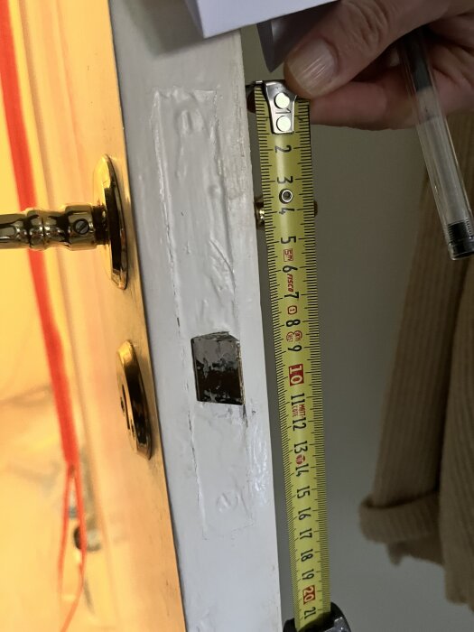 Mäta dörrkarmen med måttband för låskistinstallation på toalettdörr. Hand håller måttbandet vid kanten av dörren.