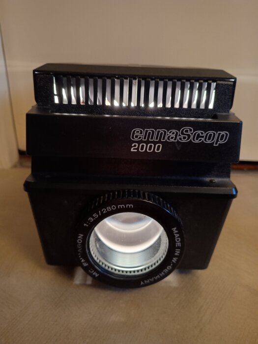 Gammal diaprojektor "ennaScop 2000" för att projicera pappersbilder; används i mörklagda rum för bättre bildvisning.