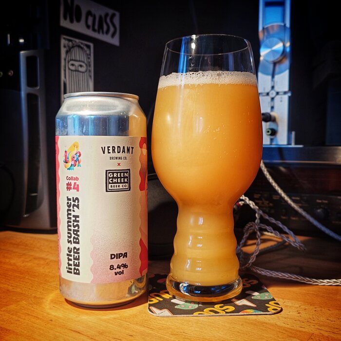 Burk och glas med DIPA-öl från Verdant Brewing Co., ställda på ett bord med "No Class" dekoration i bakgrunden.