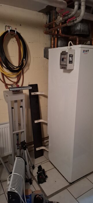 Värmepanna IVT 290 A/W i källare med kopparrör och anslutningar; utrustning och verktyg på golvet, inklusive stativ och värmefläkt.