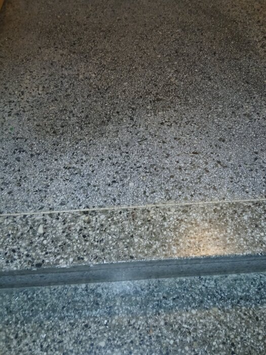 Grått terrazzogolv i en trappuppgång från 1957, med tydlig stenstruktur och steg.