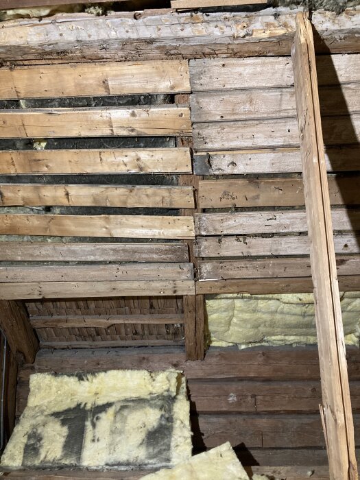 Oisolerat tak med synligt trävirke och glasfiberisolering med svart sotmärken från tidigare kamin.