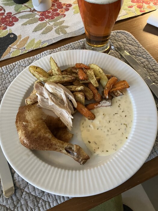 Kyckling från lergryta med rostade rotsaker och rosmarinsås serveras på en tallrik, med ett glas öl i bakgrunden.