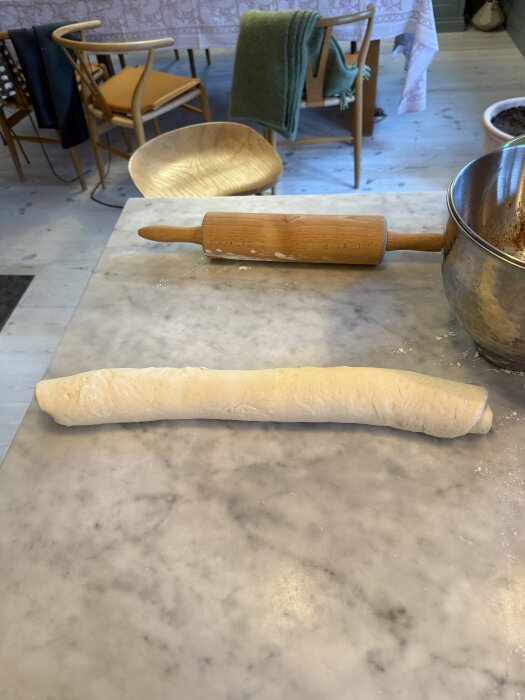Deg rullad till en rulle på en marmorbänk med en kavel och bunke intill, troligen en del av kanelbullebakning.