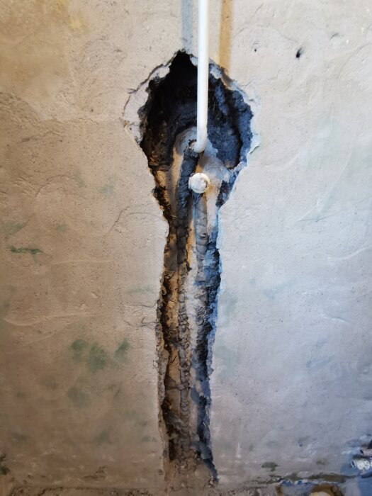 Öppen vägg med ett kopparrör synligt, omgivet av skadad puts. Rörgenomföring i badrumsrenovering.