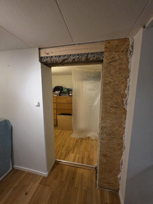 “Uppsågad dörröppning i betongvägg, ovankant behöver öppnas 5-6 cm. Synlig träplanka och plastskynke i bakgrunden.”