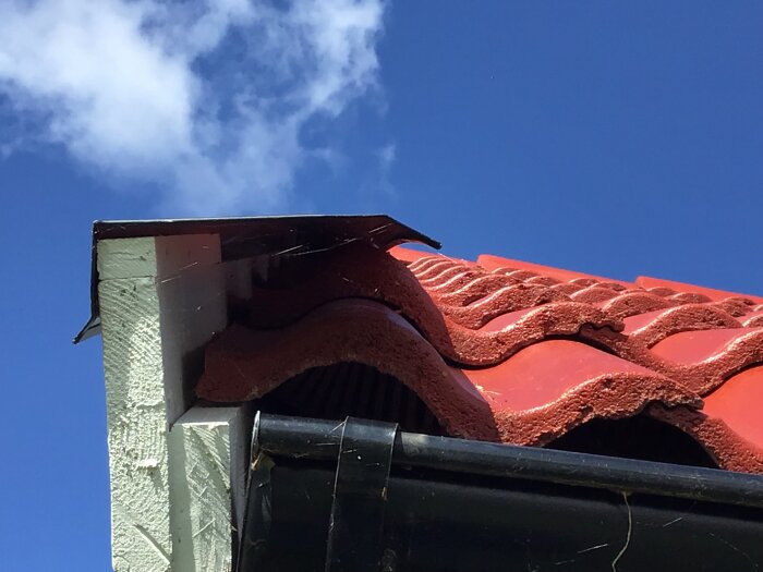Närbild av ett takhörn med röda takpannor och svart hängränna; plåten verkar inte vila på vindskivan.