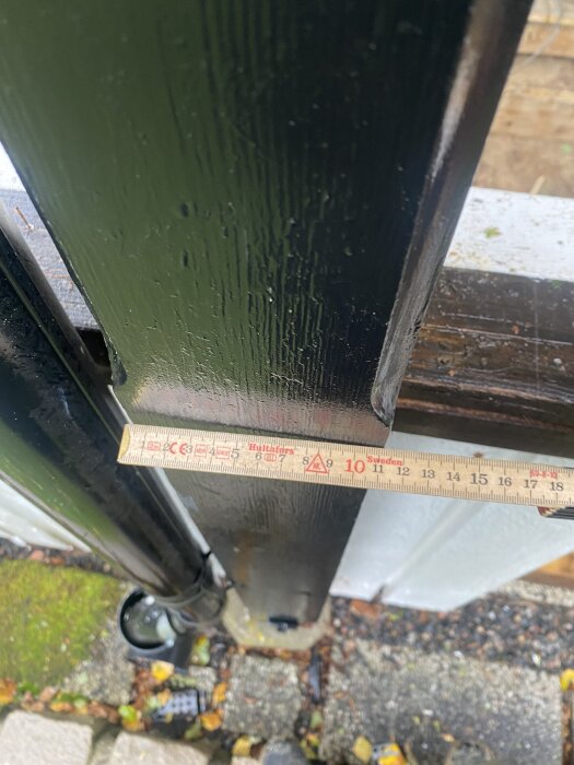 Uppmätning av en grön stolpe för ett uterum, med en linjal som visar cirka 9 cm bredd.