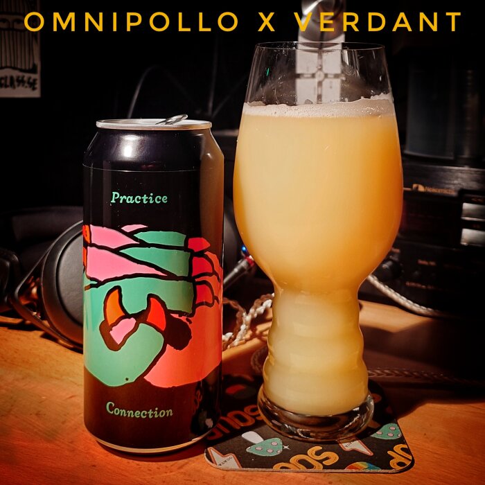 En Omnipollo x Verdant ölburk och ett glas med ljus, grumlig öl står på ett bord.