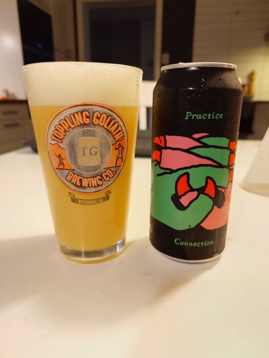 Ett glas öl från Toppling Goliath Brewing Co. bredvid en färgglad burk med texten "Practice Connection" på ett bord.