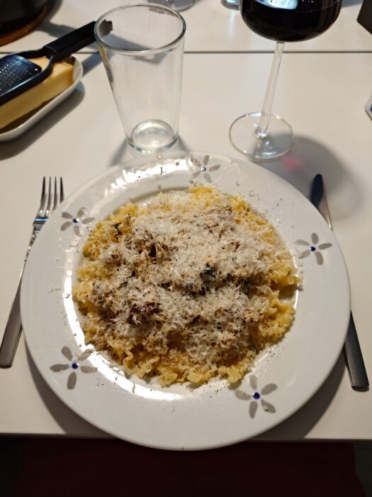 Tallrik med basilikakyckling, soltorkade tomater och pasta, toppad med riven parmesan, bredvid ett glas rött vin.