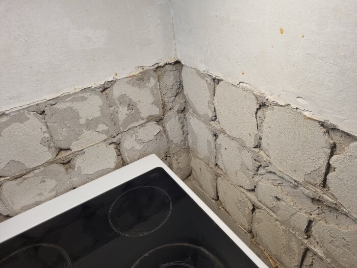 Vägg i kök med borttaget kakel, exponerad murbruksyta med ojämnheter och hål. Elspisens häll syns i bildens nedre kant.