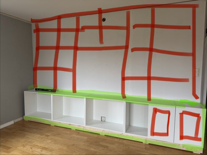 Skiss av bokhylla på vägg med röda linjer och grönt markerade ytor för MDF-klädsel. Golv i trä. Förberett utrymme för TV.
